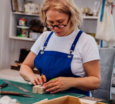 A female carpenter marks details with a pencil and cuts wood with a knife in a carpentry or homemade workshop.Workplace. Production of wooden toys.の写真素材