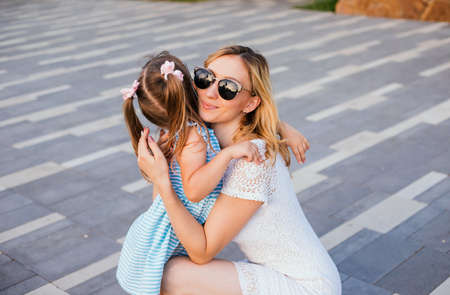 A young mother hugs her little daughter in the park. A woman in sunglasses. Entertainment and pampering of the child. A fun summer walk in the park.の写真素材