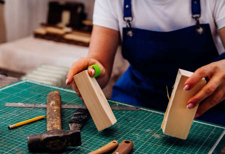 A female carpenter cuts wood with a knife in a carpentry or makeshift workshop. Dust and shavings...