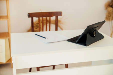 A computer tablet on a white desktop and a piece of paper with a pencil. workplace. The bright interior of the room.の写真素材
