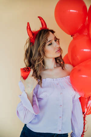 A young woman with red horns and heart-shaped balloons and a gift box. The concept of the March 8...