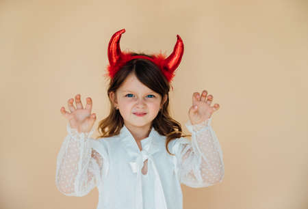 Portrait of a little girl in a white dress with devil horns. Halloween costume. Angry mood. A menacing expression on his face.の写真素材