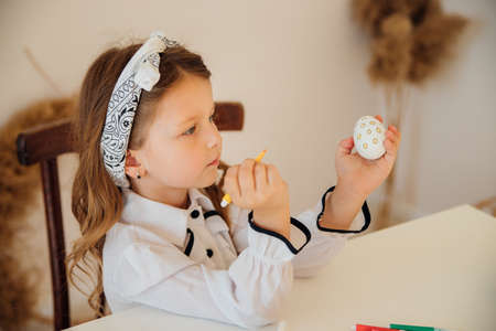 A girl decorates an Easter egg.The child draws with a felt-tip pen on an egg, focused on the...
