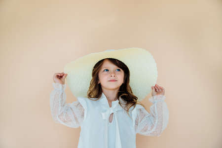 Beautiful little girl in a straw hat, beach style for kids.Time for vacations and happy summer holidays.A girl on a beige, neutral background.の写真素材