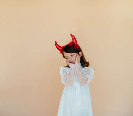 Portrait of a little girl in a white dress with devil horns. Halloween costume. Angelic facial expression. The concept of two different personalities in character.の写真素材