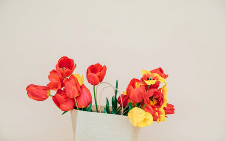 A beautiful composition of spring flowers. A bouquet of red tulips in a paper bag on a beige...