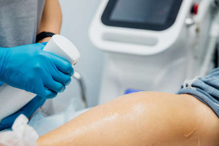 A master or cosmetologist in blue gloves prepares the client's skin, preparing for the epilation procedure. The concept of body care. beauty salon. Moisturizing and nourishing the legs.の写真素材