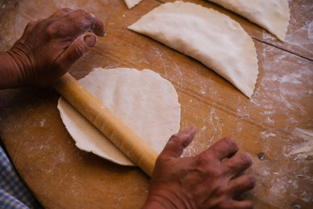 Female hands holding a rolling pin in the process of cooking kutaba or chebureks, minced meat and...