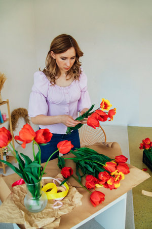 A young woman is packing a festive bouquet in wrapping paper. The florist makes an assembly with red tulips in the workshop. A woman at work, in a small business or hobby.の写真素材
