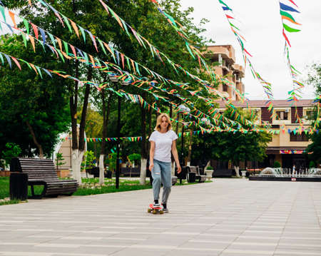 A young beautiful teenage girl rides a skateboard on a beautiful summer day in the park. A girl enjoys skateboarding outdoors. An active lifestyle.の写真素材