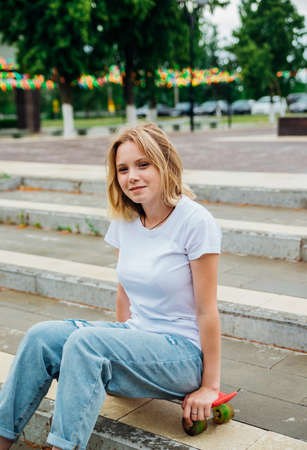 Portrait of a teenage girl in casual clothes in the park. Summer skateboarding, active lifestyle. A student or a schoolboy is sitting on a skateboard during the summer holidays. sports recreation.の写真素材