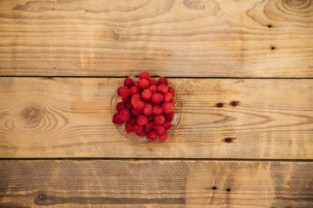 Raspberry fruits on a small saucer, a bunch of summer berries on a wooden background. summer...