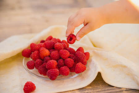 A small saucer with ripe raspberries, a bunch of summer berries on a wooden background. A child's...