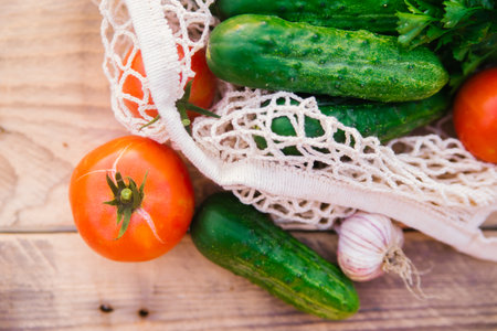 Fresh juicy vegetables, products in a reusable shopping bag, a string bag made of recycled materials, on a wooden table in the garden. Vegetarianism. No plastic. Eco-friendly lifestyle.の写真素材