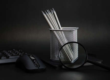 Silver colored pencils, magnifying glass and notepad on a black background. Minimalistic and monochrome photography style. The theme of office, work, training, career.の写真素材