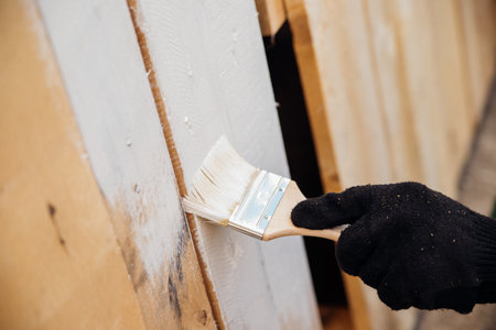 A gloved hand paints a wooden background and boards.Painting works indoors and outdoors. Renovation of premises. The brush is dipped in white paint.の写真素材