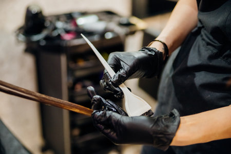 Close-up of a woman's head in the process of hair coloring in a beauty salon. Close-up of a woman's hands in black gloves coloring her hair with a brush. Kerating of hair.の写真素材