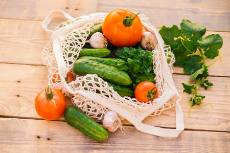 Fresh juicy vegetables, products in a reusable shopping bag, a string bag made of recycled materials, on a wooden table in the garden. Vegetarianism. No plastic. Eco-friendly lifestyle.の写真素材