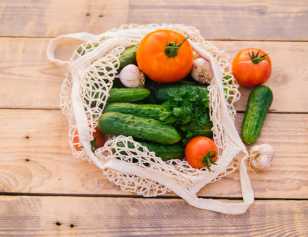 Fresh juicy vegetables, products in a reusable shopping bag, a string bag made of recycled materials, on a wooden table in the garden. Vegetarianism. No plastic. Eco-friendly lifestyle.の写真素材