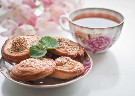 Puff cookies with sesame seeds on plate and english tea