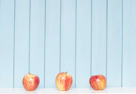 tree red apples on the shelf on blue wooden backgroundの写真素材