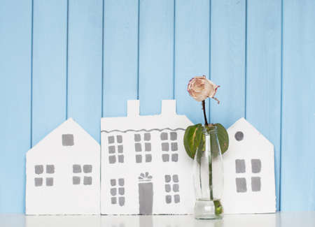 three wooden houses and  white rose in the bottle on the bookshelf  on blue backgroundの写真素材