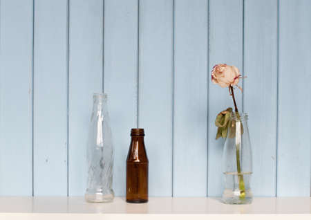 three old bottles with white dry rose on the home bookshelf on blue wooden background