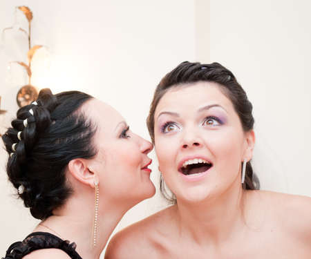 Young woman tells her friend a big secretの写真素材