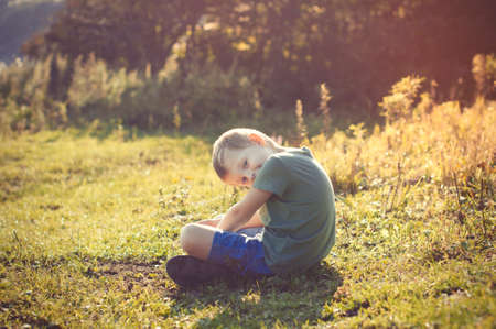 Young healthy smiling little child is sitting on the grass in park, sunny summer wonderful dayの写真素材