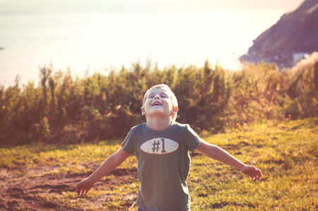 Happy cheerful smiling little child walking in the autumn park on a sunny day and enjoying wonderful successful life and warm weatherの写真素材