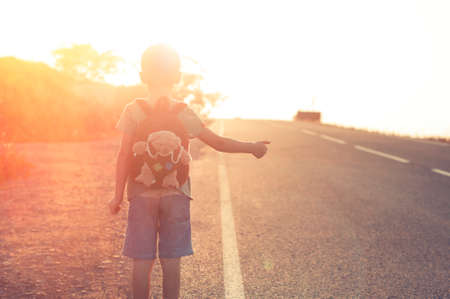 Lost child standing on the road hitchhiking on a sunsetの写真素材