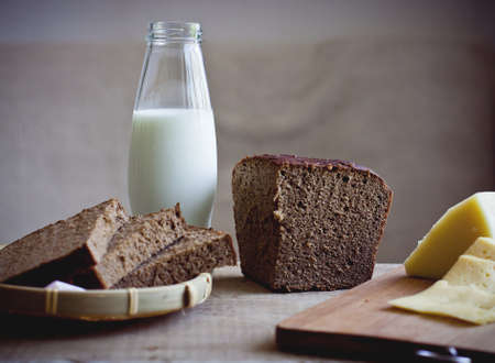 Food still life with sliced cheese, rye brown bread and bottle of fresh milkの写真素材