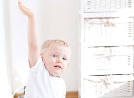 boy is raising up his hand in white interiorの写真素材