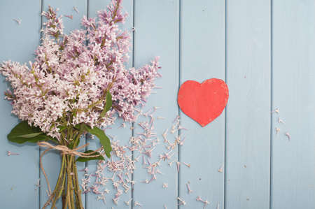 Red wooden heart and summer blooming bouquet of lilac on blue wooden backgroundの写真素材