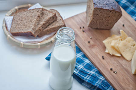 Bottle of milk, cheese and rye brown bread on rustic gingham table clothの写真素材