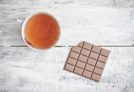 Cup of tea and bar of milk chocolate on white wooden tableの写真素材