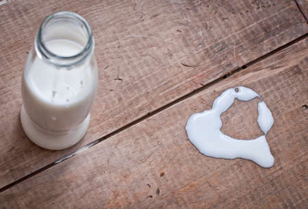 milk in glass bottle and heart shaped symbol on wooden tableの写真素材