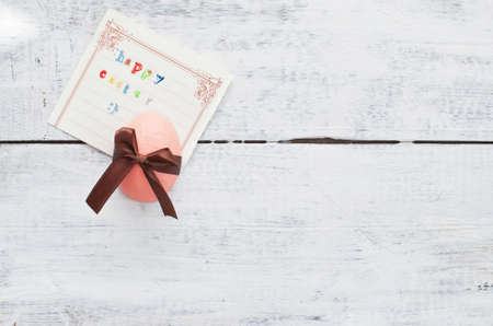 easter egg decorated with ribbon and card on wooden backgroundの写真素材