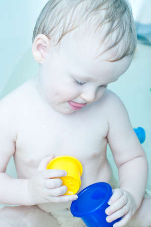 little cute blue eyed boy is taking a bath and playing with cupsの写真素材