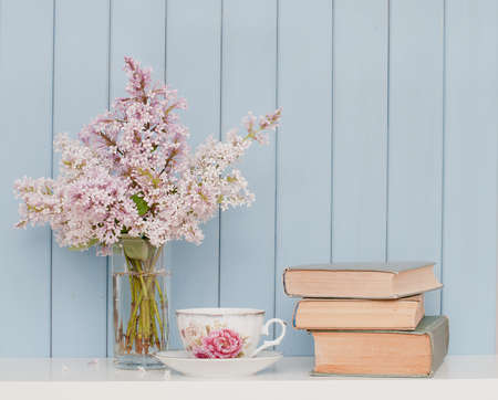 Gentle bunch of lilac, vintage books and china teacup on the table on blue wooden backgroundの写真素材