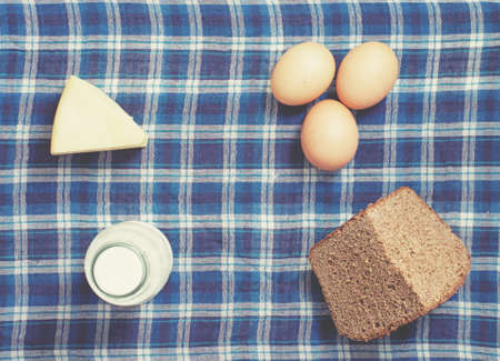 hen eggs, bottle of milk, rye bread, cheese on gingham table clothの写真素材