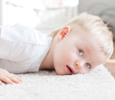 cute little boy is lying on the white carpetの写真素材