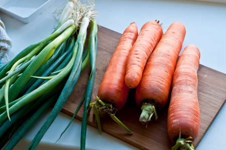 Fresh vegetables, carrots and spring onion on cutting board on old wooden tableの写真素材