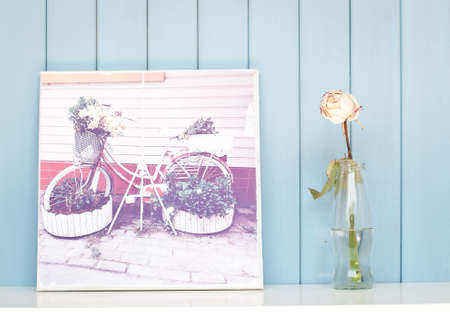 Vintage poster and single rose in glass bottle in the bookshelf on blue wooden backgroundの写真素材
