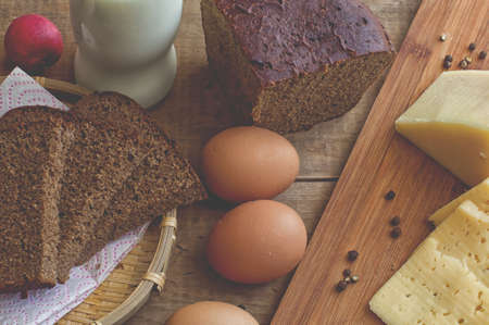 Red radish, bottle of milk, rye bread, cheese, hen eggs on wooden tableの写真素材