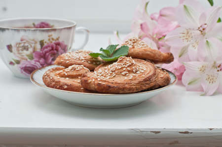 Homemade bakery, puff cookies with sesame seeds on plate, english tea and tender beautiful flowersの写真素材