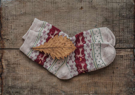 Knitted woolen warm socks and dry yellow oak leaf on wooden backgroundの写真素材