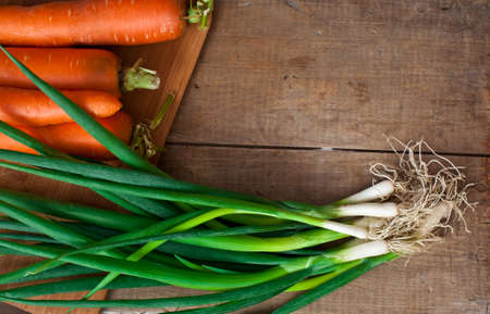 Fresh vegetables, carrots and spring onion on cutting board on old wooden table