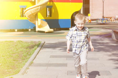 happy little kid is running on the children's playground in bright sunny summer dayの写真素材
