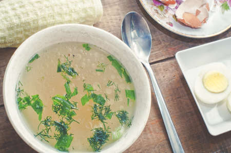 Chicken soup in bowl, spoon, eggs, eggshell on rustic wooden tableの写真素材